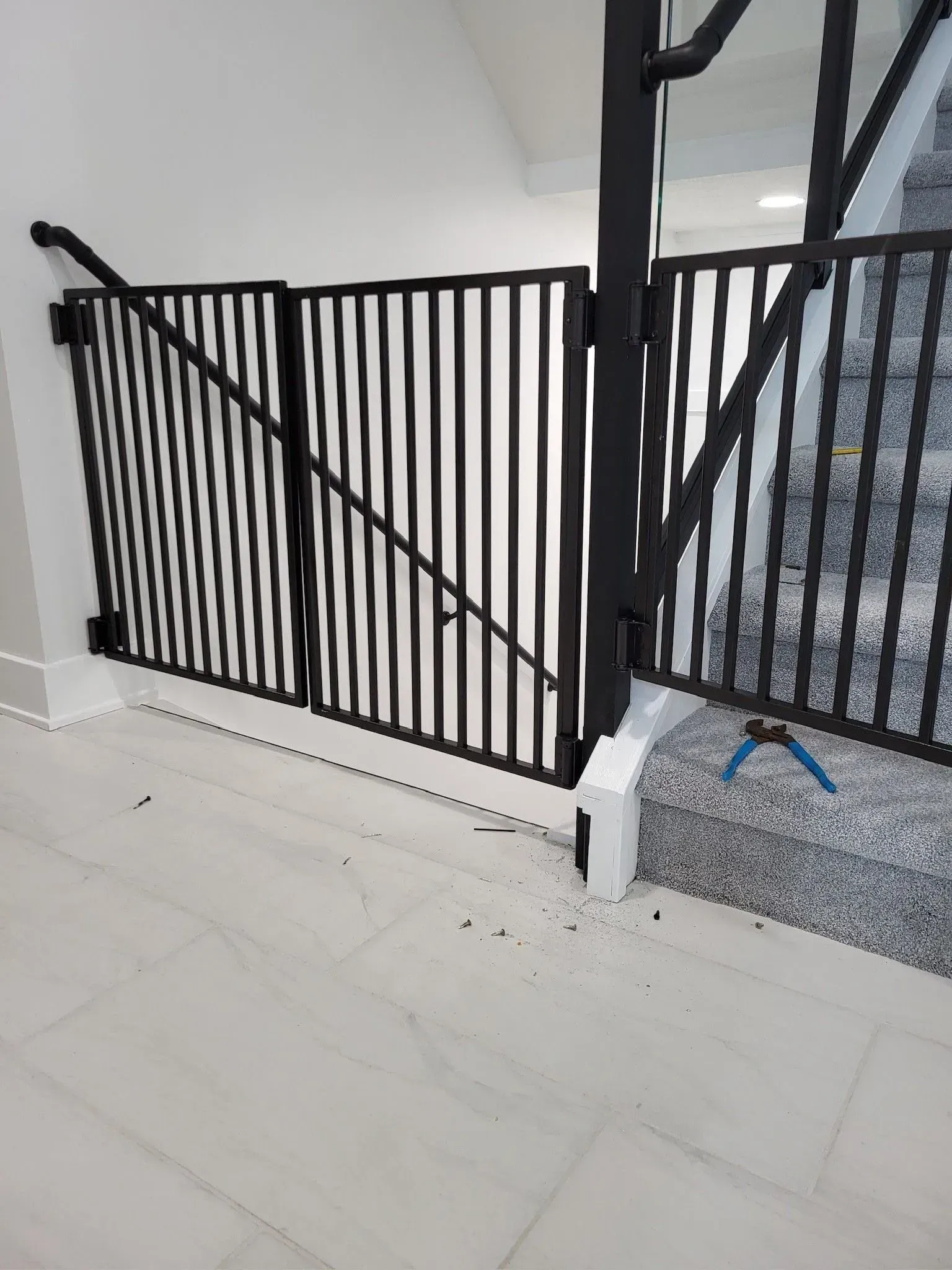 Black metal safety gate at top of stairs, white walls and floor.