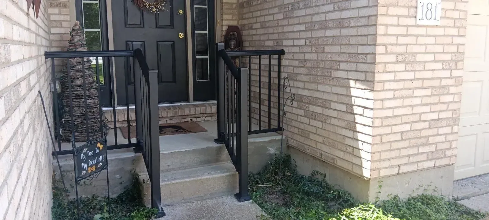 A front entrance with black railing and steps leading to a black door, with brick siding.