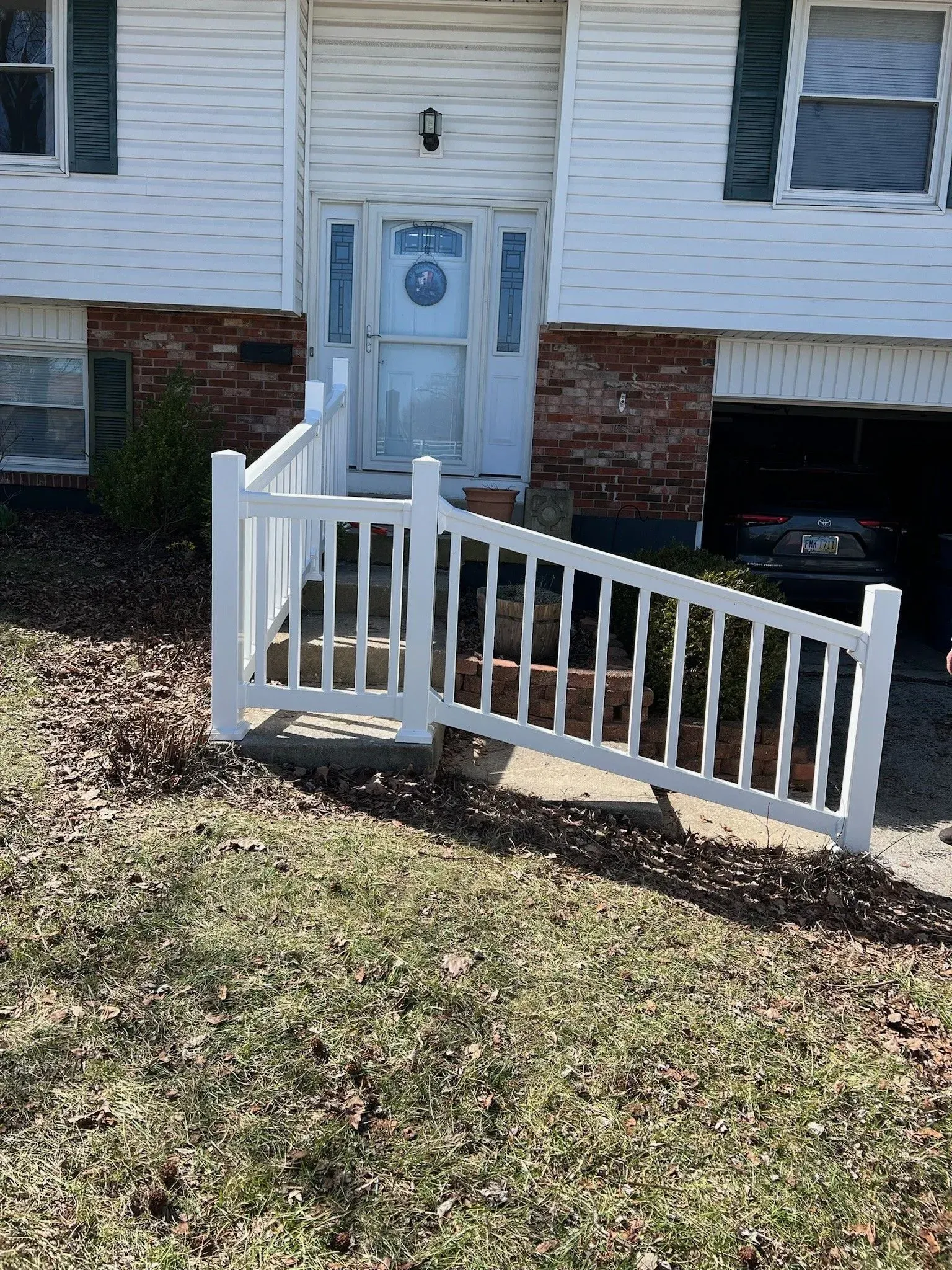 White vinyl fence in front of a house. Entrance door visible with brick accents, and a garage on right side.