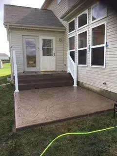 Brown stamped concrete patio with steps leading to a door and windows.