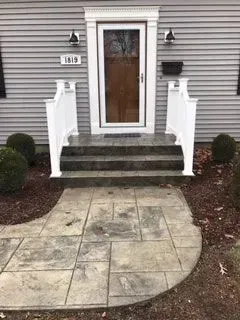Exterior view of a house with a concrete walkway leading to the front door, flanked by steps and landscaping.