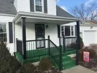 White house with a green porch, black railing and trim.