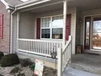 Beige home porch with white railing, window, red shutters, and front door.