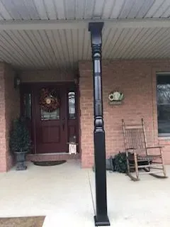 Black porch post on a brick house with a dark red door and a wreath.