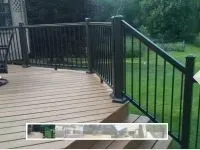 Brown deck with dark railing overlooking a green lawn.
