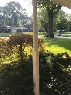 View from a porch with a white column, overlooking a lawn, trees, and houses.