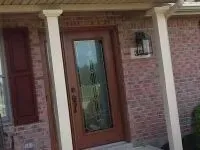 Brick house with brown door, glass window, and white columns.