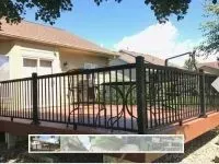 Black railing surrounds a wooden deck with patio furniture in front of a house.