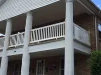 Two-story brick building with white columns and balcony, white railing.