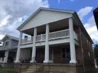 Two-story brick house with a white columned porch and balcony under a cloudy sky.