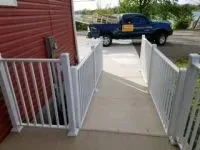 Ramp with white railing next to a red building. A blue truck is parked in the background.