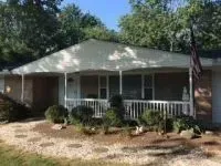 Ranch-style house with a covered porch, white railing, and American flag. Landscaping includes bushes and stepping stones.