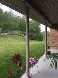 View from a porch with white columns overlooking a grassy yard and trees.