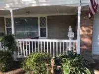 Porch with white railing, brick wall, and American flag; bushes in front.