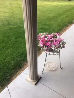 Column on concrete, next to a metal plant stand with pink and white flowers. Lawn in background.