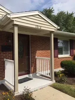 Exterior view of a brick home with a small porch, featuring beige pillars and white railing. Number 
