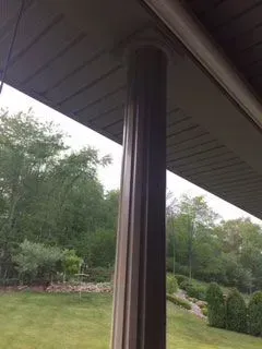 Brown fluted column supports a porch roof. Trees and lawn are in the background.