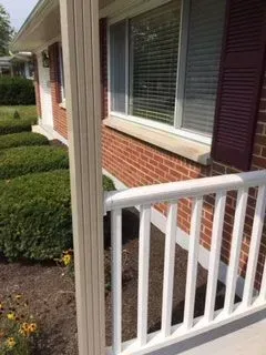 Beige porch column, white railing, red brick exterior, window with closed blinds.