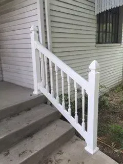 White railing on concrete steps leading to a light-colored house.