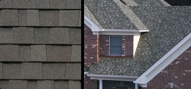 Close-up of asphalt roof shingles, next to a brick house with a dark gray roof.