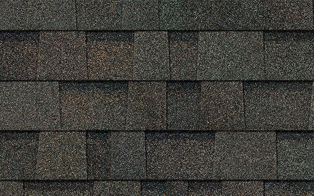 Close-up of asphalt roof shingles in shades of brown and gray, textured with granular coating.