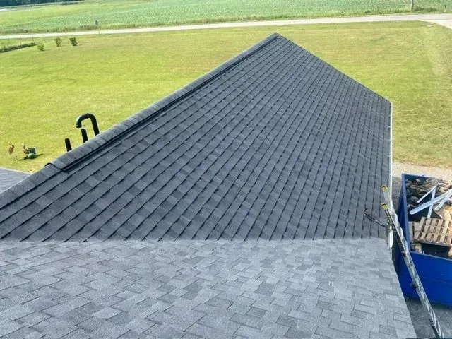 Newly shingled dark gray roof on a building, with a grassy field in the background.