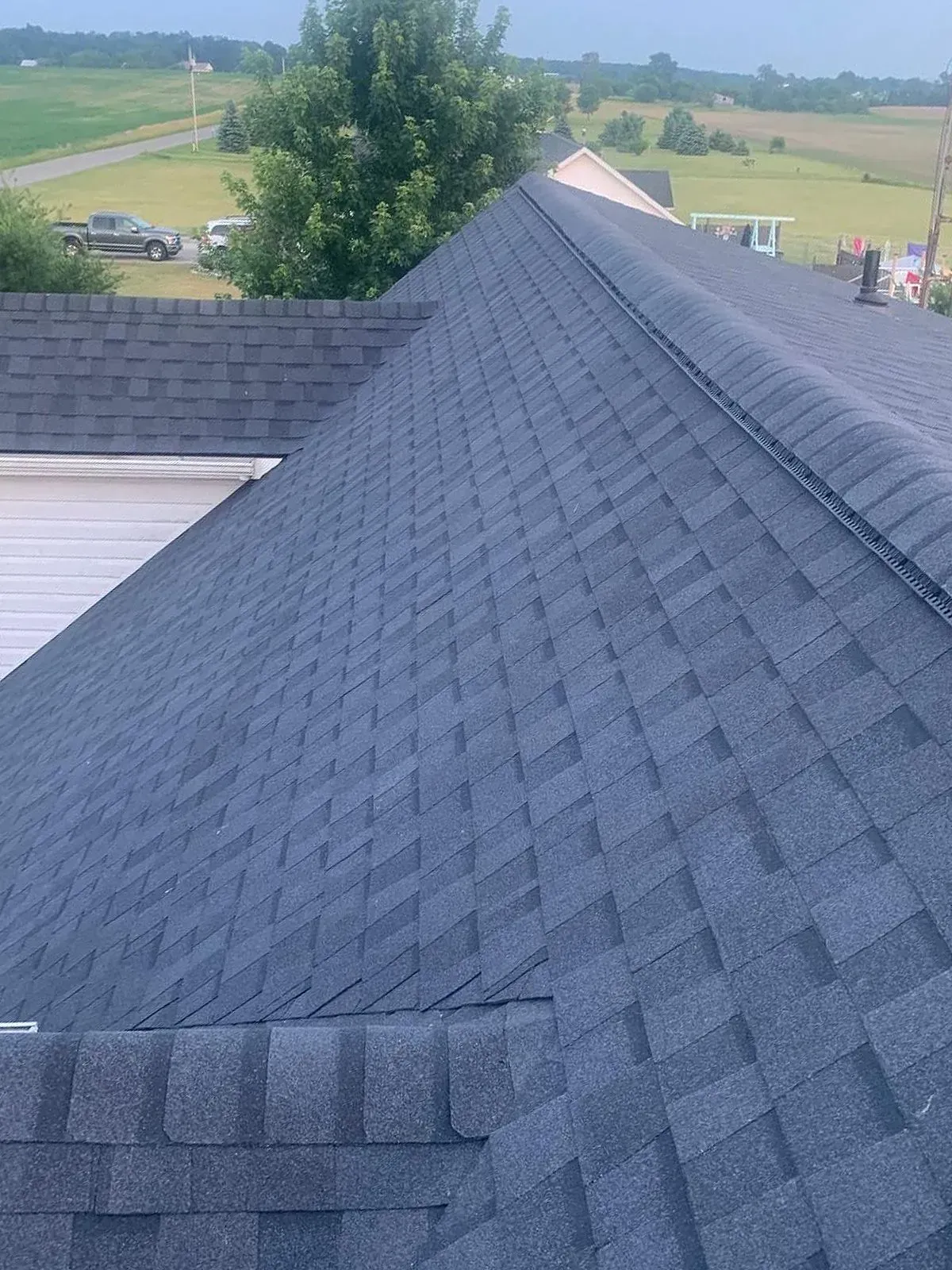 Dark gray shingle roof on a building, angled view. Distant field and blue sky.