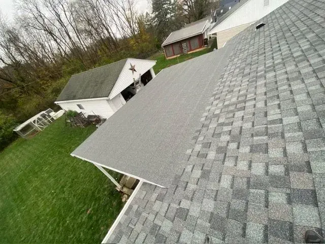 Gray asphalt shingle roof on a house, with a green yard and other buildings in the background.