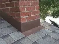 Brick chimney with brown flashing on a shingle roof.