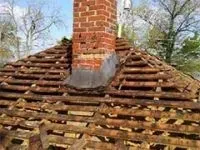 Roof of a house with visible wooden rafters and a brick chimney. The roof is partially dismantled.