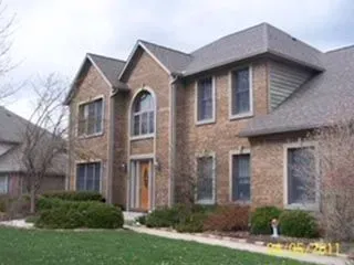 Brick two-story house with multiple windows and a front lawn; a cloudy sky is visible.