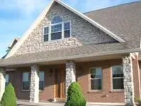 House with stone and brick exterior, windows, and small bushes in front.