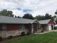 Red-sided house with gray roof, brick and stone facade, garage, and green lawn under a cloudy sky.