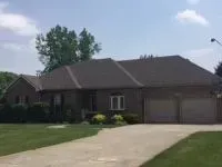 Brick ranch house with brown roof and two-car garage on a sunny day.