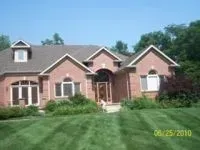 Brick house with arched doorway, dormer, and manicured lawn under blue sky.