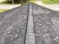 Dark grey asphalt shingle roof, ridge cap, and faded appearance, viewed from above.