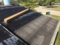 Black roofing material being installed on a roof with a wooden beam on top.
