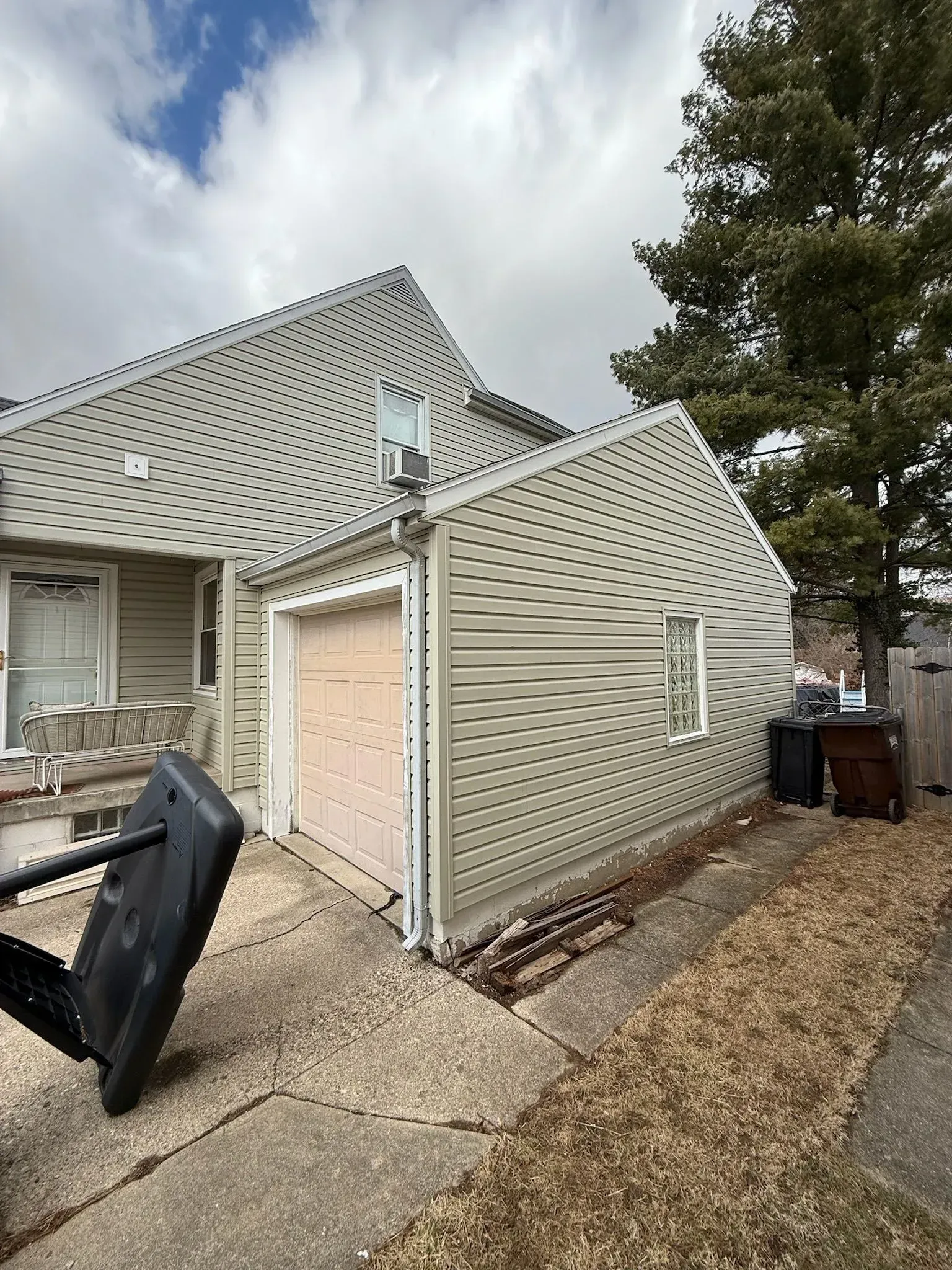 House with attached garage, beige siding, pink garage door, overcast sky. Basketball hoop in foreground.