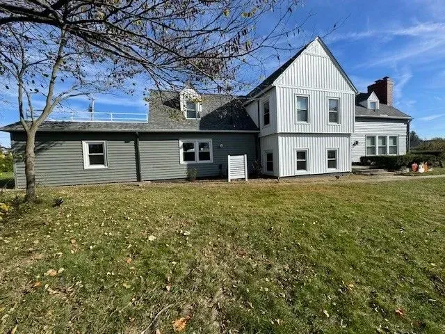 A gray and white house with a gabled roof, set in a grassy yard under a blue sky.