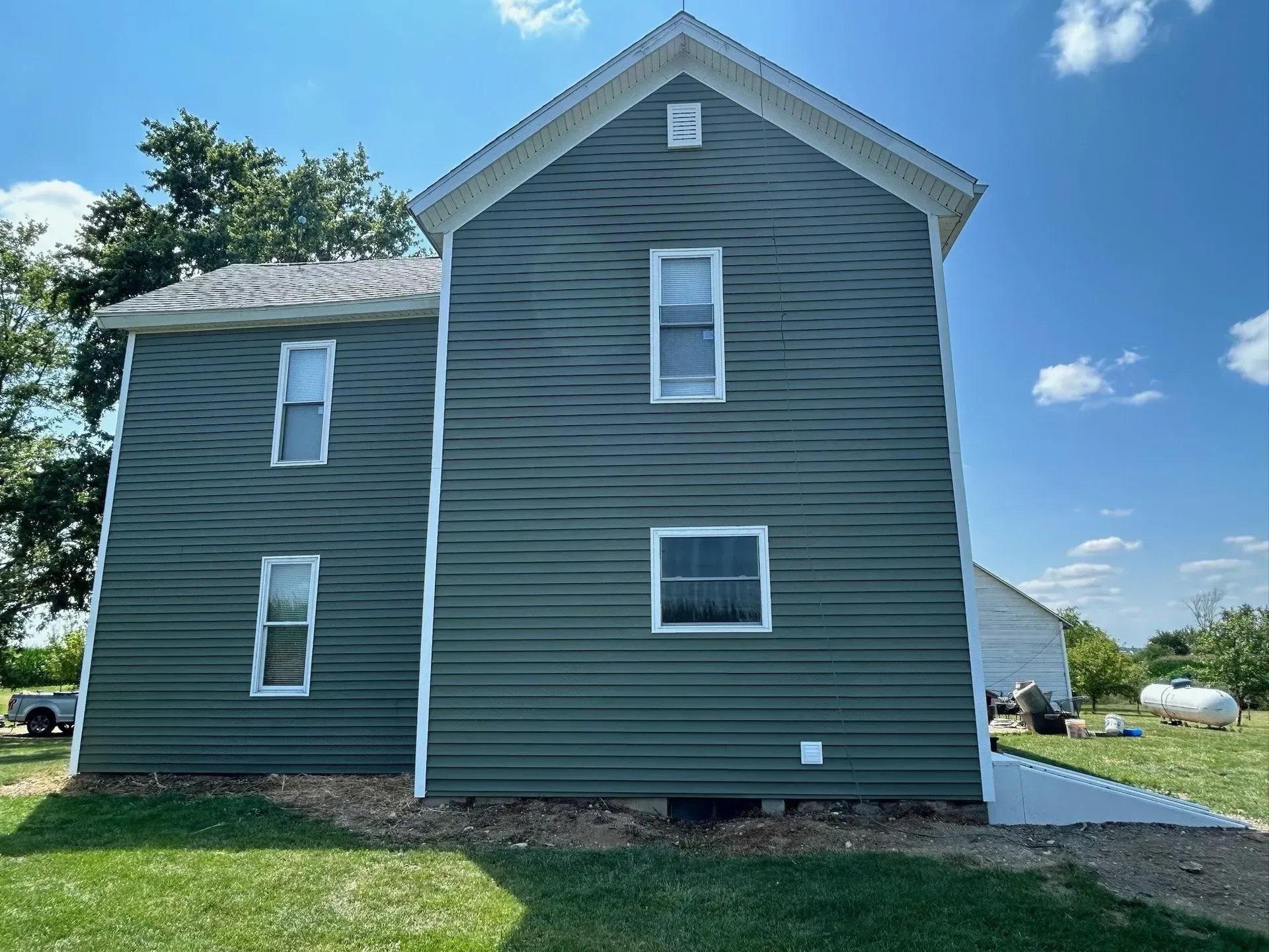 Side view of a two-story house with green siding and white trim against a blue sky with clouds.