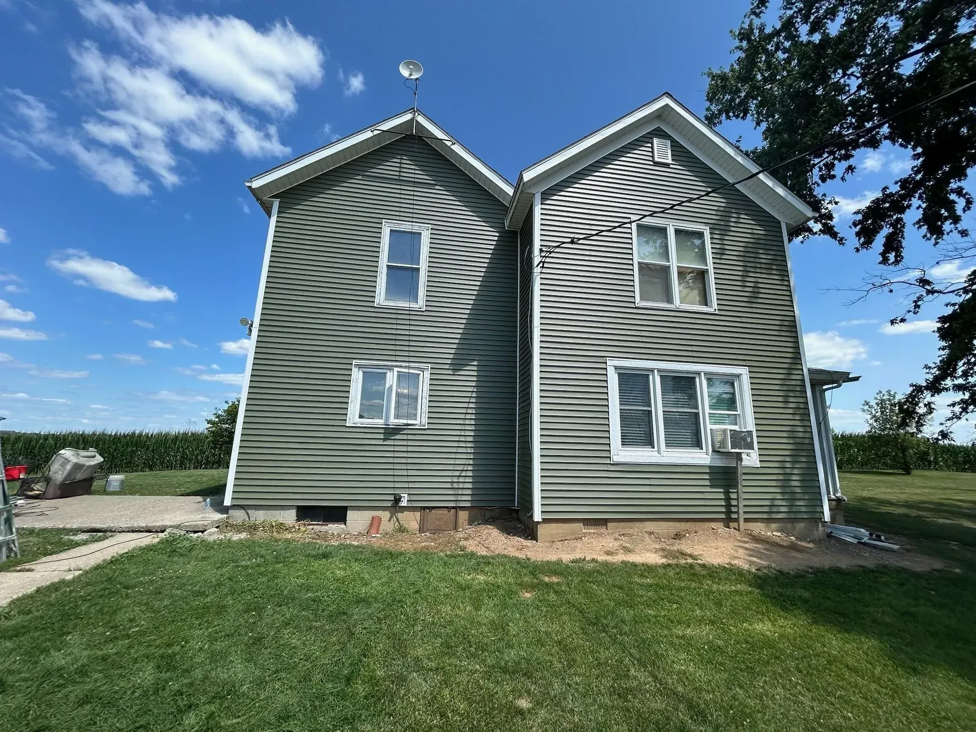 Two-story green house with white trim against a bright blue sky with some trees and green grass.