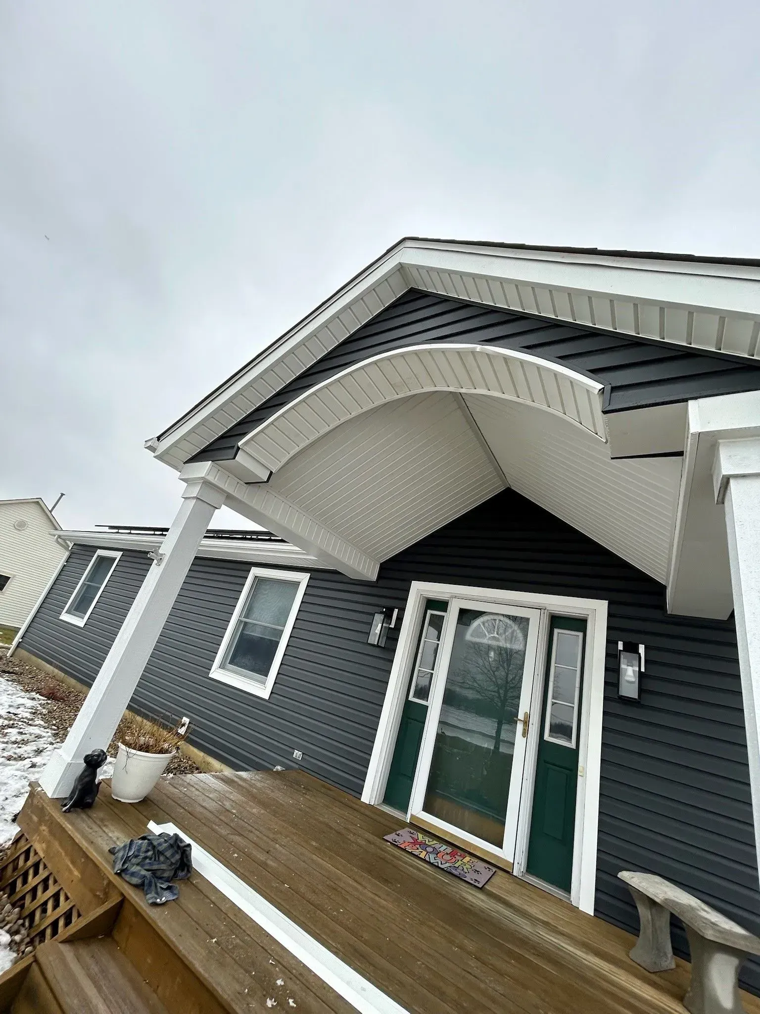 A gray house with a white porch overhang. Dark siding, snow, and a wooden deck are visible.