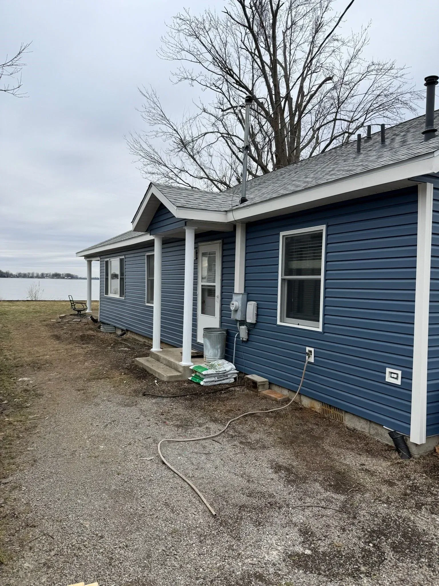 Blue-sided cottage with white trim near a body of water. Overcast day.