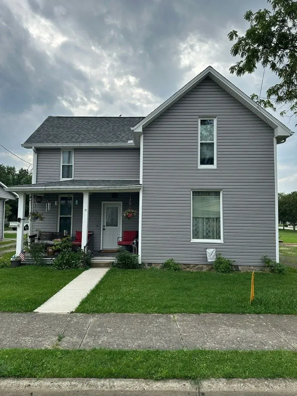 Gray two-story house with white trim, porch, and grass lawn under a cloudy sky.