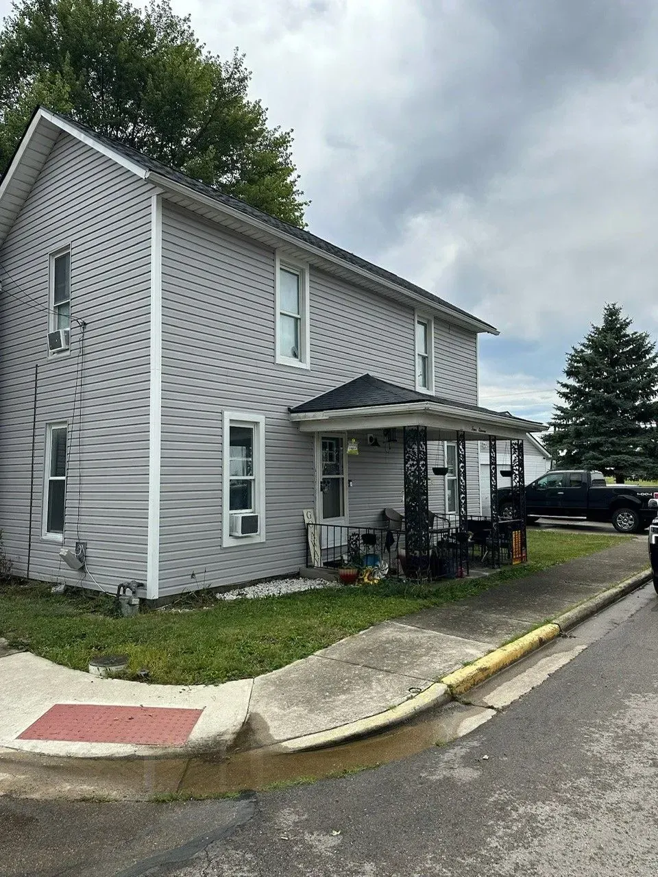 Two-story light gray house with a porch and grass lawn on a cloudy day.