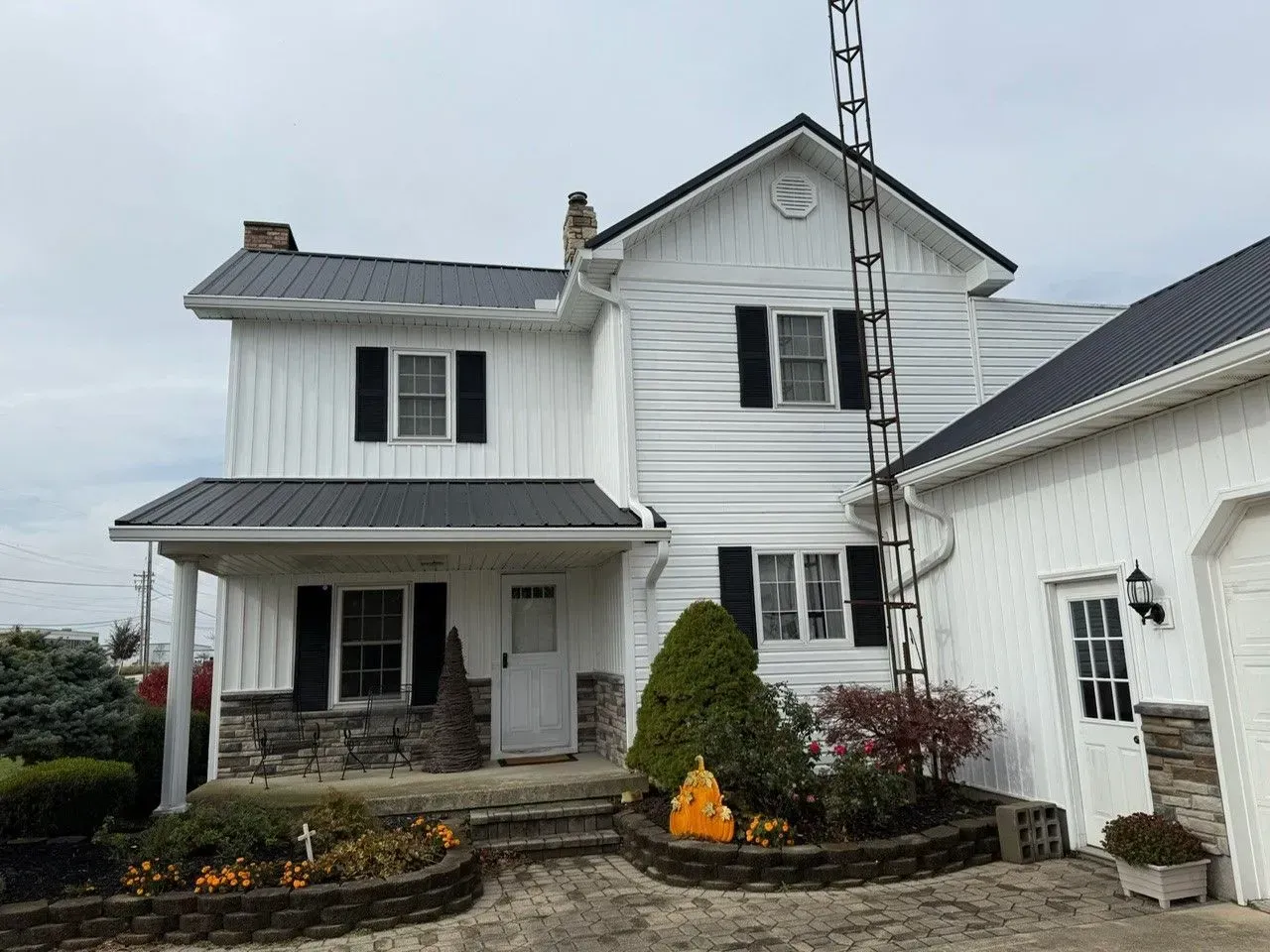 White farmhouse with black shutters and roof, stone accents, and a radio tower on a cloudy day.