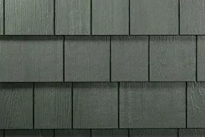 Close-up view of dark green square-shaped shingles, forming a textured wall surface.