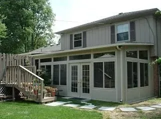 Beige two-story house with screened-in porch and wooden deck. Green lawn and stepping stones in the yard.