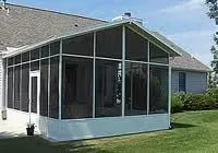 Screened-in porch addition with white frame, black screens, attached to a gray house on a green lawn.
