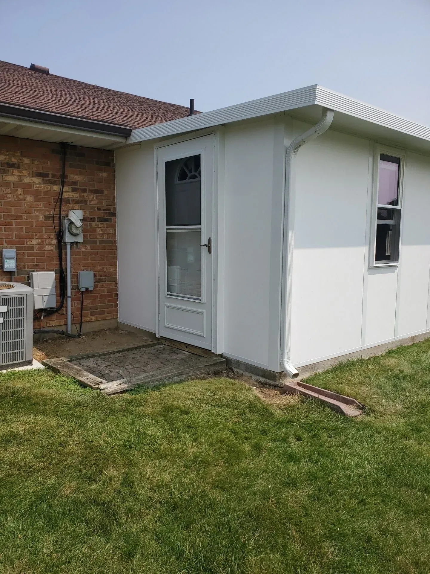 White sunroom addition attached to a brick building, with a door, window, and metal roof.